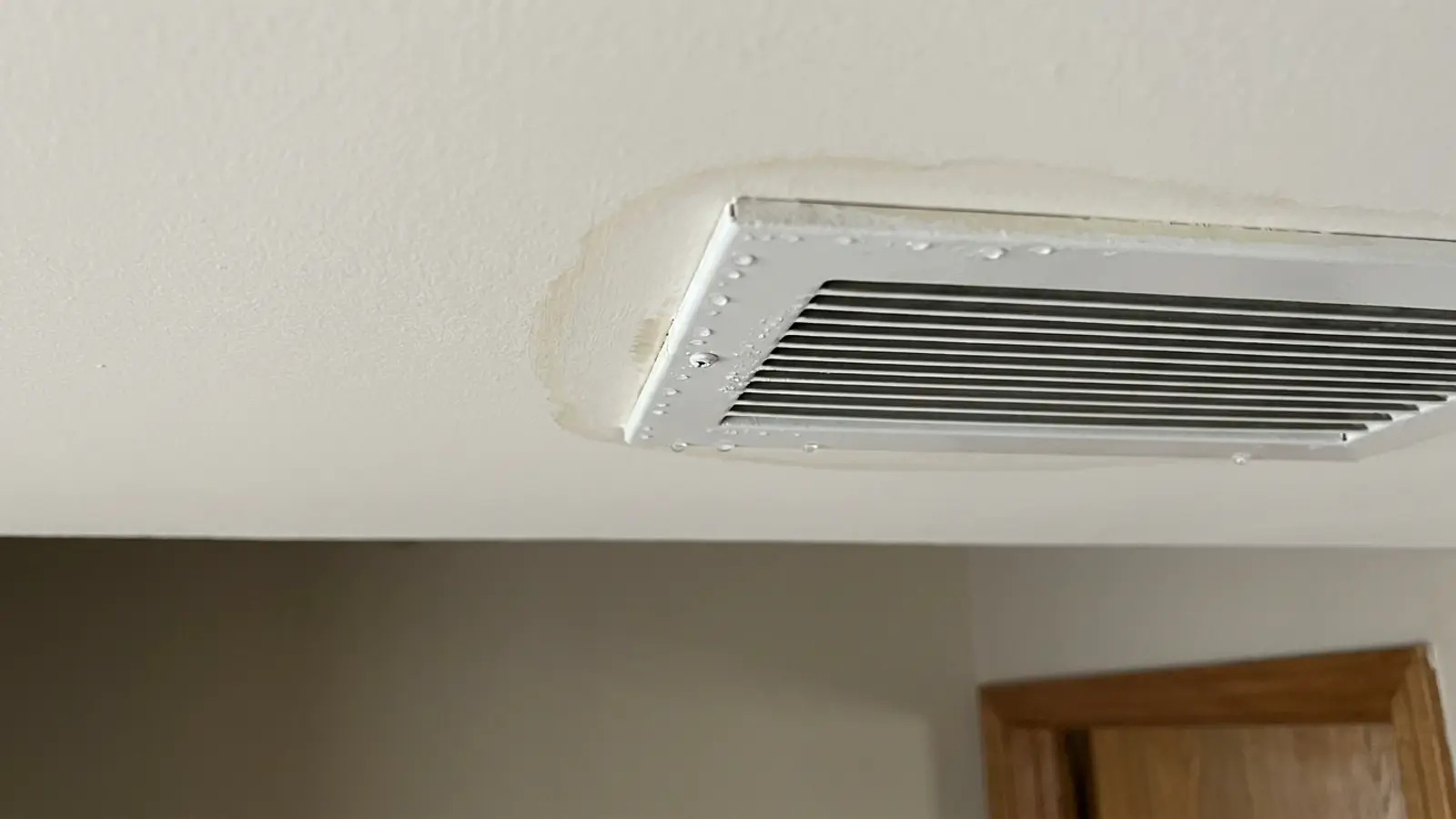 Moisture beading and a faint stain around the edges of a white ceiling supply register