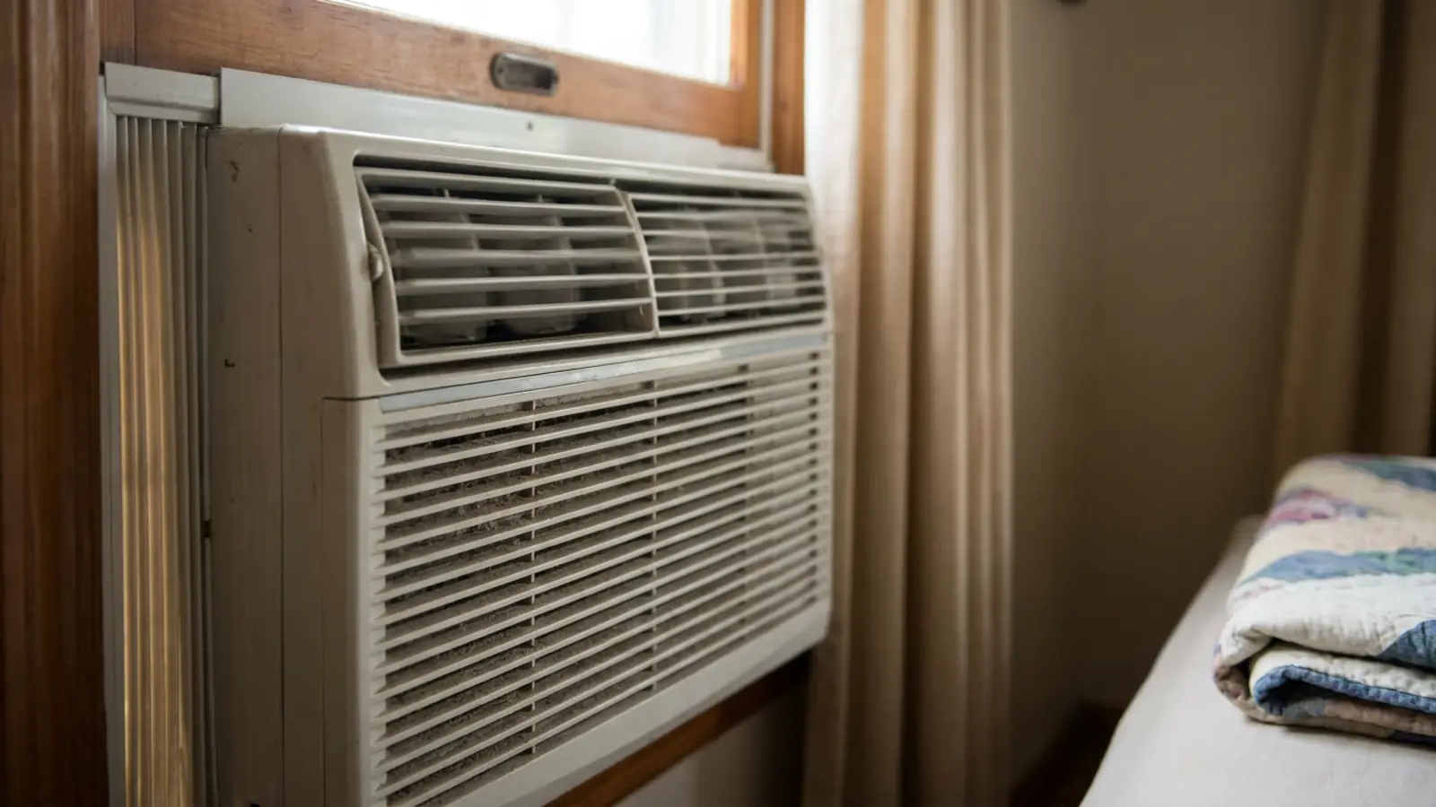 A close-up of the vibrating front grille of a window air conditioner installed in a bedroom window